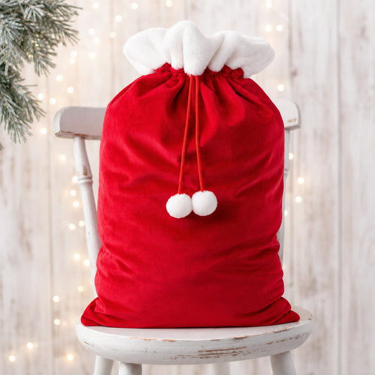Red plain large Santa sack with white faux fur trim, drawstring and pom poms on a rustic white chair - wholesale blank for sublimation, embroidery, HTV and DTF, KWC1649R