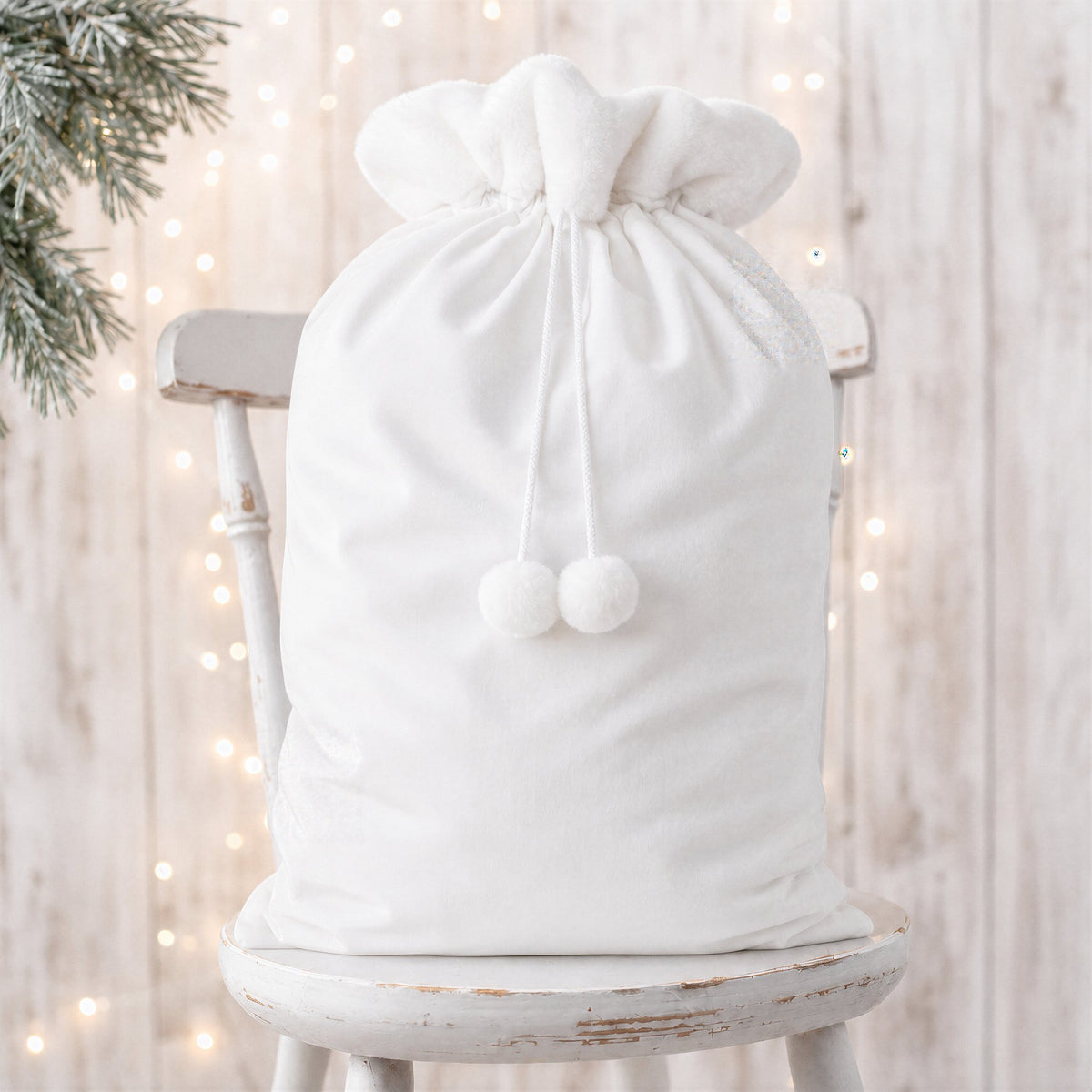 White plain large Santa sack with white faux fur trim, drawstring and pom poms on a rustic white chair - wholesale blank for sublimation, embroidery, HTV and DTF, KWC1649W