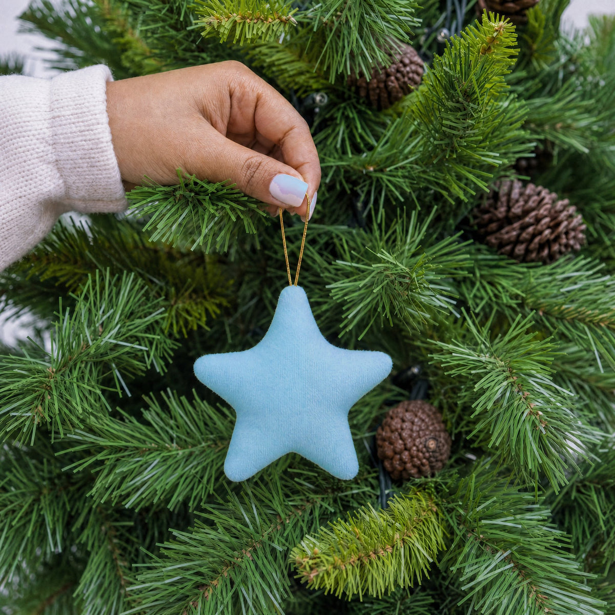 Light blue plush fabric star shape Christmas decoration with gold hanging string being hung on a Christmas tree - wholesale blank for personalisation, KWC2407LB